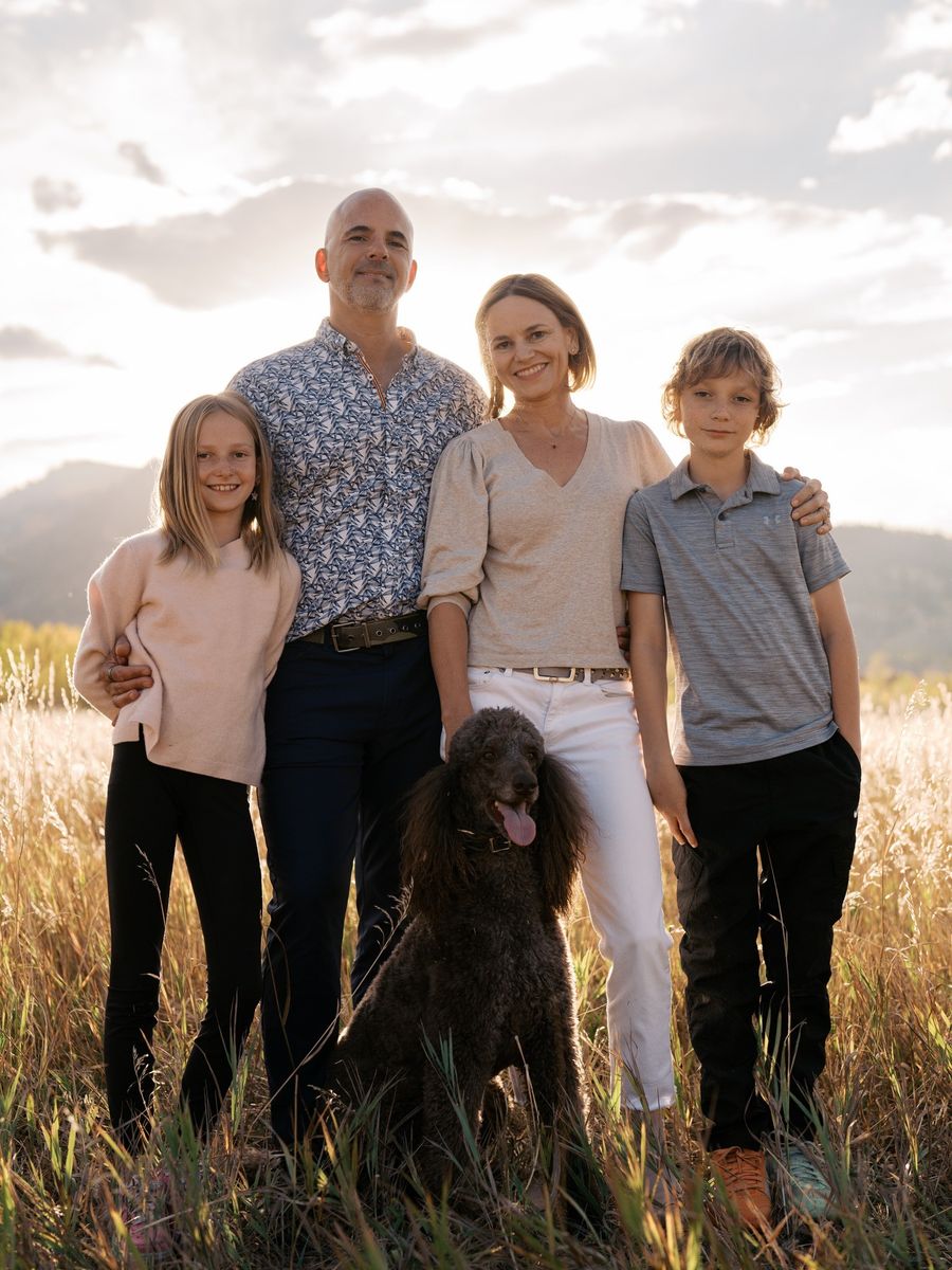 Chris with his wife, their twins and a black poodle in a sunlit meadow