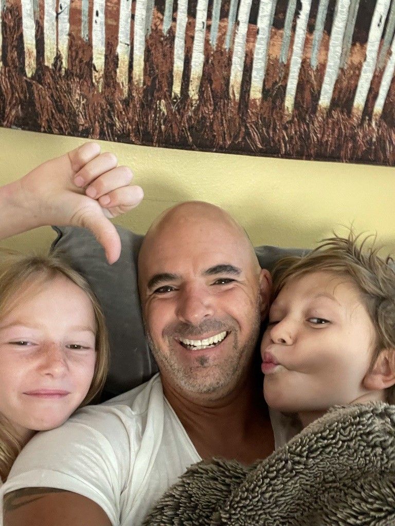 A selfie of Chris grinning between the twins, one giving a thumbs-down, the other making a kissy face
