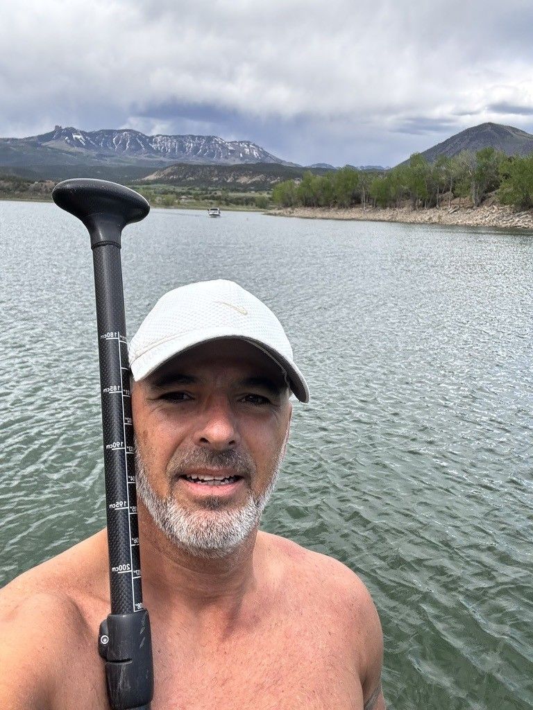 Chris on a mountain lake holding a paddle, mountains behind