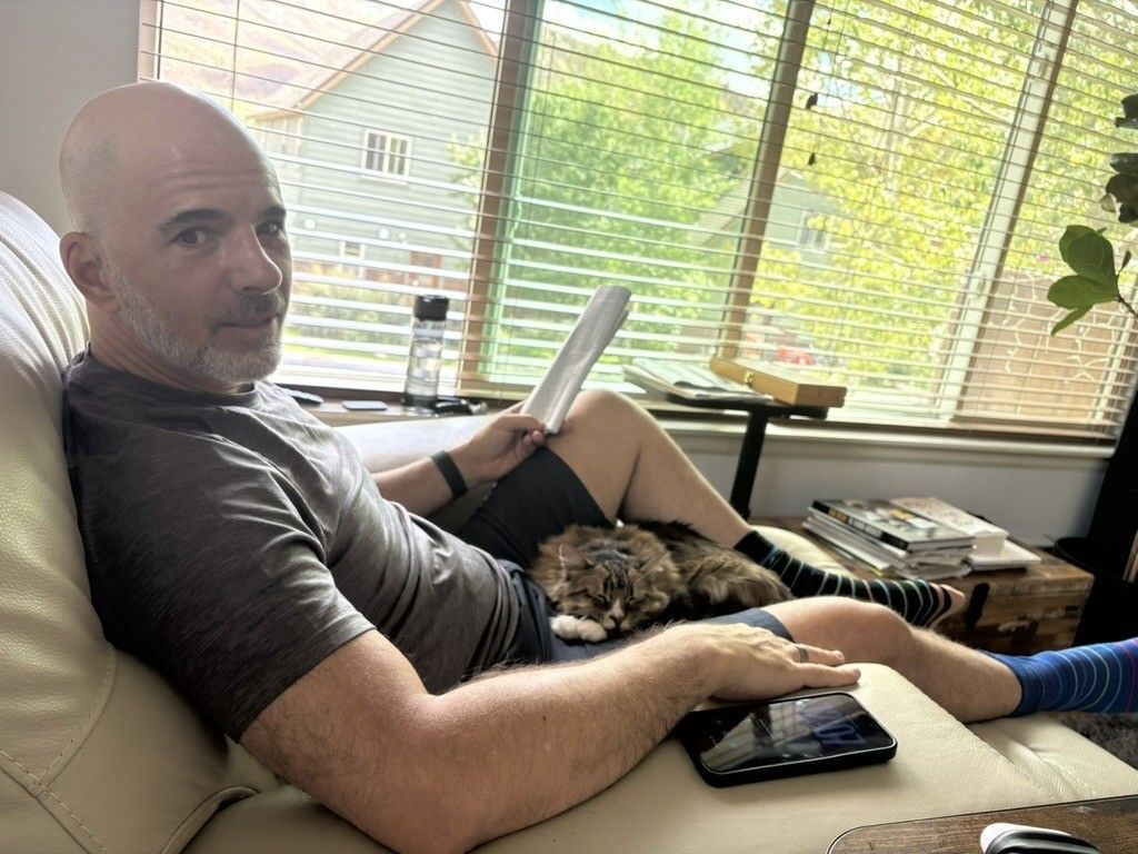 Chris reading in an armchair by a window, a cat asleep on his lap